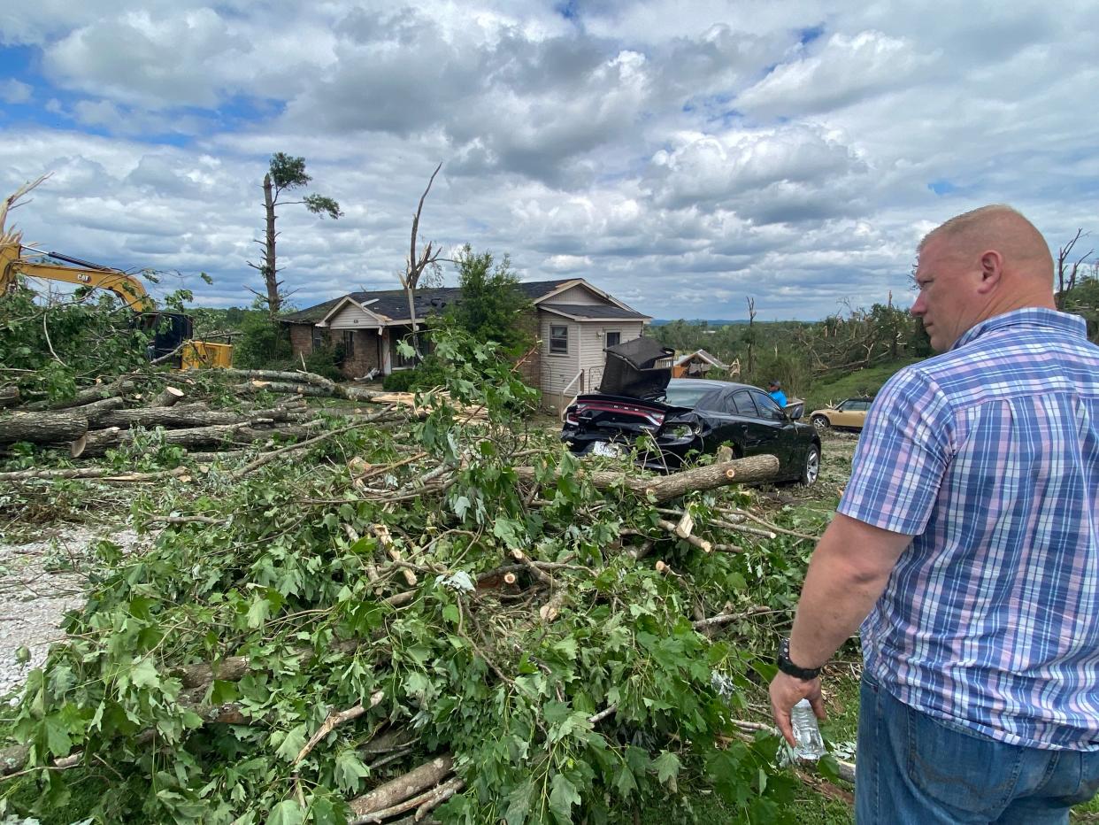 Sam Barnes watches and waits as an excavator readies to remove the front overhang of from his home that was damaged in Wednesday’s tornado.