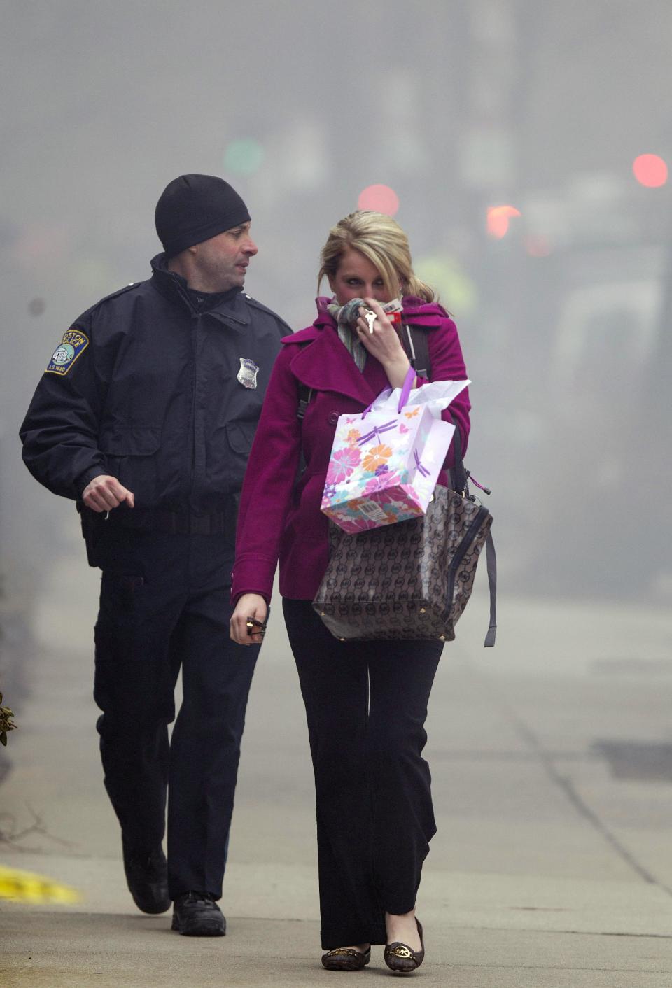 A Boston Police officer escorts a woman away from the scene of a multi-alarm fire at a four-story brownstone in the Back Bay neighborhood near the Charles River, Wednesday, March 26, 2014, in Boston. Boston EMS spokesman Nick Martin says four people, including at least three firefighters, have been taken to hospitals. (AP Photo/Scott Eisen)