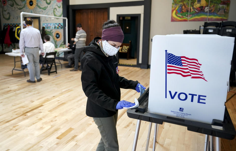 Shanon Hankin, cleans a voter booth after it was used for voting at the Wil-Mar Neighborhood Center Tuesday,  April 7, 2020 in Madison, Wis.  Voters across the state are ignoring a stay-at-home order in the midst of a pandemic to participate in the state's presidential primary election. (Steve Apps/Wisconsin State Journal via AP)