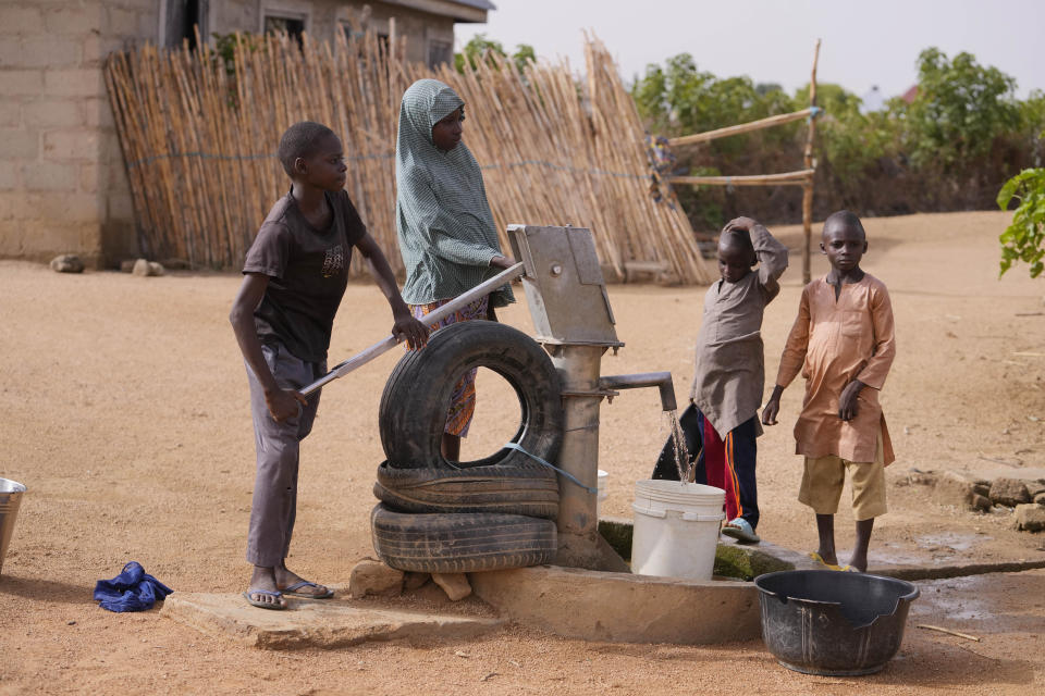 Hauwa Bwami's grandson Suleiman, right, who nearly lost his life to kwashiokor, andt others fetch water at a borehole in Kaltungo Poshereng Nigeria, Sunday, June 2, 2024. More than a dozen women gathered this week in Kaltungo's Poshereng village where they are learning at least 200 recipes they can prepare with those local foods which, in the absence of rain, are grown in sand-filled sacks that require small amounts of water. The training session mirrored the struggles of households who are more challenged amid Nigeria's worst cost of living crisis. (AP Photo/Sunday Alamba)