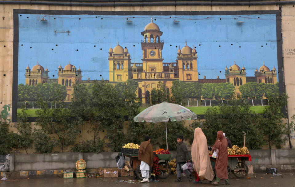 A family walk past a huge mural of historical Islamia College building painted on an overhead bridge wall, in Peshawar, Pakistan, Friday, Jan. 7, 2022. An international watchdog said Friday, June 17, it will keep Pakistan on a so-called “gray list” of countries that do not take full measures to combat money-laundering and terror financing but raised hopes that its removal would follow an upcoming visit to the country to determine its progress.(AP Photo/Muhammad Sajjad)