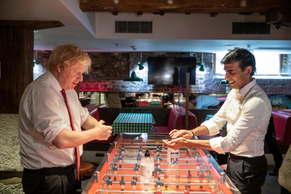 Britain's Prime Minister Boris Johnson (L) and Britain's Chancellor of the Exchequer Rishi Sunak use hand sanitizer on either side of a table football game as they visit Pizza Pilgrims in West India Quay, London Docklands on June 26, 2020 as the restaurant prepares to reopen on July 4 as coronavirus lockdown rules are eased. - The British government on Thursday unveiled plans to get the public out of indoor confinement and on to the streets to boost the economy after three months of coronavirus lockdown. Prime Minister Boris Johnson wants pubs and restaurants to be buzzing in the curtailed summer season, despite continued social distancing rules and restrictions. (Photo by Heathcliff O'Malley / POOL / AFP) (Photo by HEATHCLIFF O'MALLEY/POOL/AFP via Getty Images)