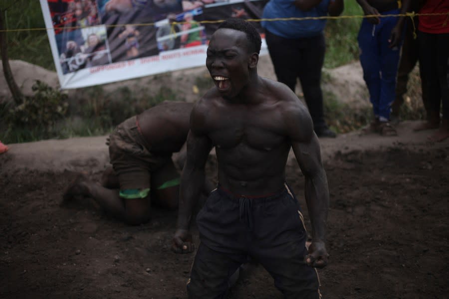 Ugandan youth celebrate after winning an amateur wrestling tangle in the soft mud in Kampala, Uganda, Wednesday, March. 20, 2023. The open-air training sessions, complete with an announcer and a referee, imitate the pro wrestling contests the youth regularly see on television. While a pair tangles inside the ring, made with bamboo poles strung with sisal rope, others standing ringside cheer feints and muscular shows of strength. (AP Photo/Patrick Onen)