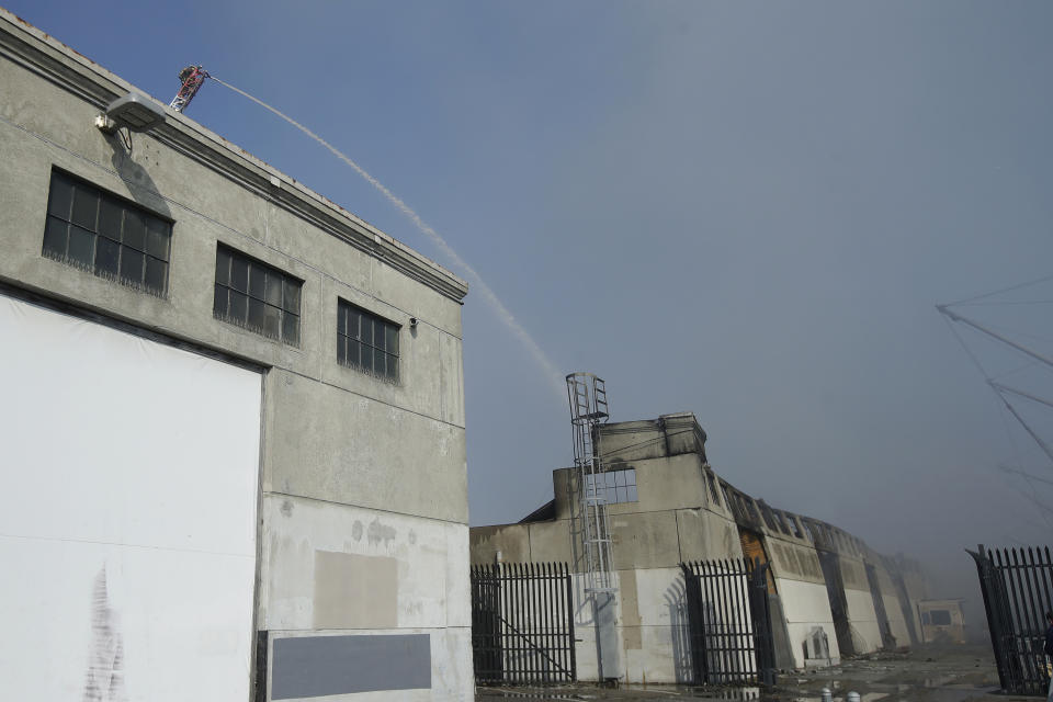 A firefighter sprays into a warehouse after a fire broke out before dawn at Fisherman's Wharf in San Francisco, Saturday, May 23, 2020. Fire officials said no injuries have been reported Saturday morning and firefighters are making multiple searches to ensure no one was inside the building on Pier 45. (AP Photo/Jeff Chiu)