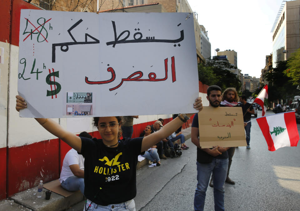 Anti-government protesters hold placards, one reads, "Down with the rule of the banks," during a protest against the central bank and the Lebanese government, in Beirut, Lebanon, Thursday, Oct. 31, 2019. Lebanese security forces were still struggling to open some roads Thursday as protesters continued their civil disobedience campaign in support of nationwide anti-government demonstrations. (AP Photo/Hussein Malla)