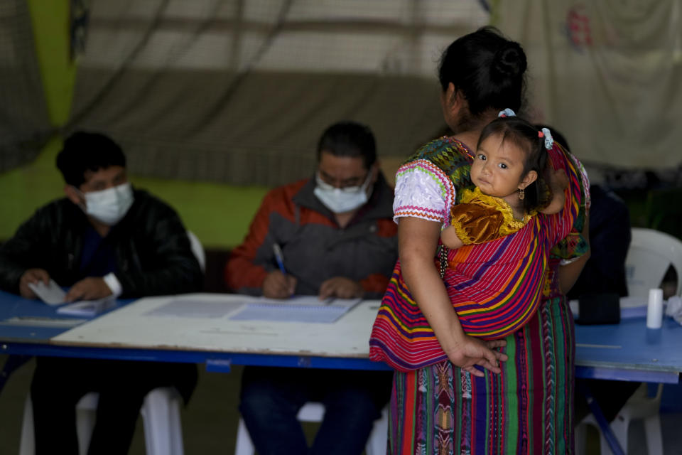 Una mujer llega a un centro de votación para votar con una niña en brazos durante la segunda vuelta de las elecciones presidenciales en Santa María Cauque, Guatemala, el domingo 20 de agosto de 2023. (Foto AP/Moisés Castillo)