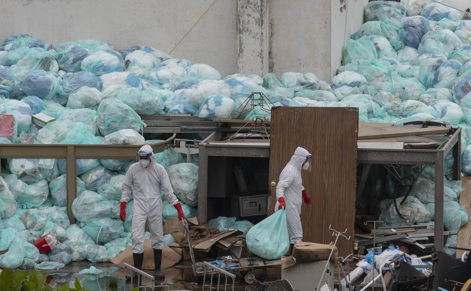 FILE - In this Aug. 12, 2020 file photo, medical workers using protective equipment dispose of trash bags containing hazardous biological waste into a large pile outside the Hospital del Instituto Mexicano del Seguro Social, which treats patients with COVID-19 in Veracruz, Mexico. According to a report released the third week of April, by the University of California, San Francisco, Mexico would have had a significantly lower COVID-19 death toll if it had reacted as well as the average government. (AP Photo/Felix Marquez, File)