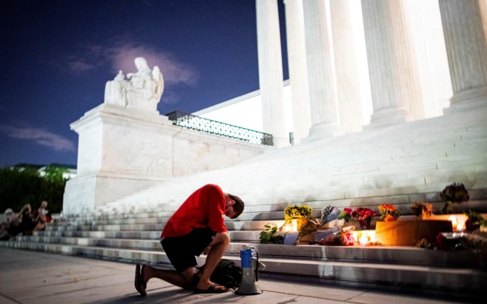 A man kneels as he brings a megaphone to a vigil on the steps of the US Supreme Court following the death of Ruth Bader Ginsburg - Reuters