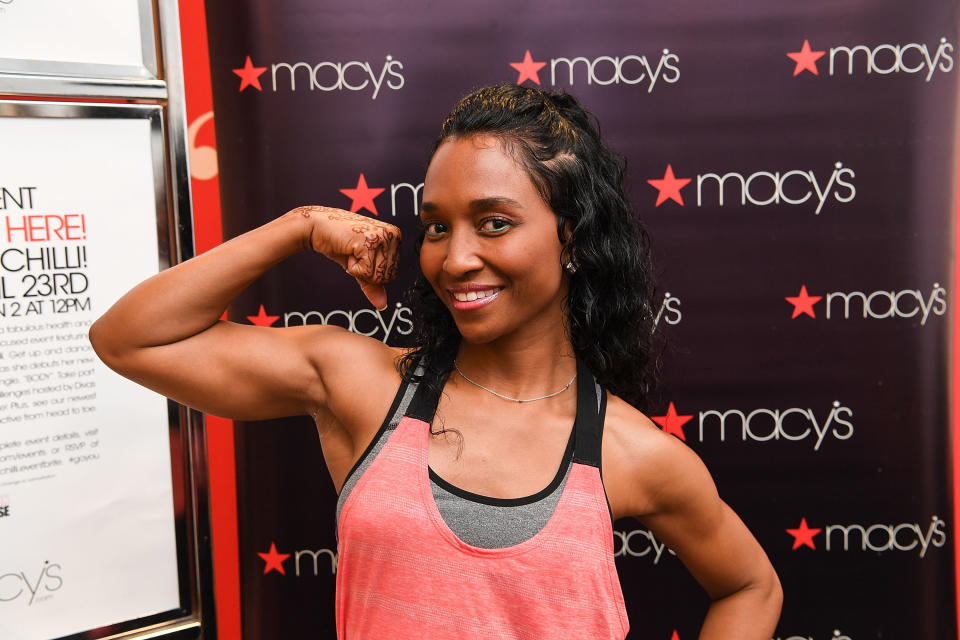 Chili, who's wearing workout clothes, flexing at an event