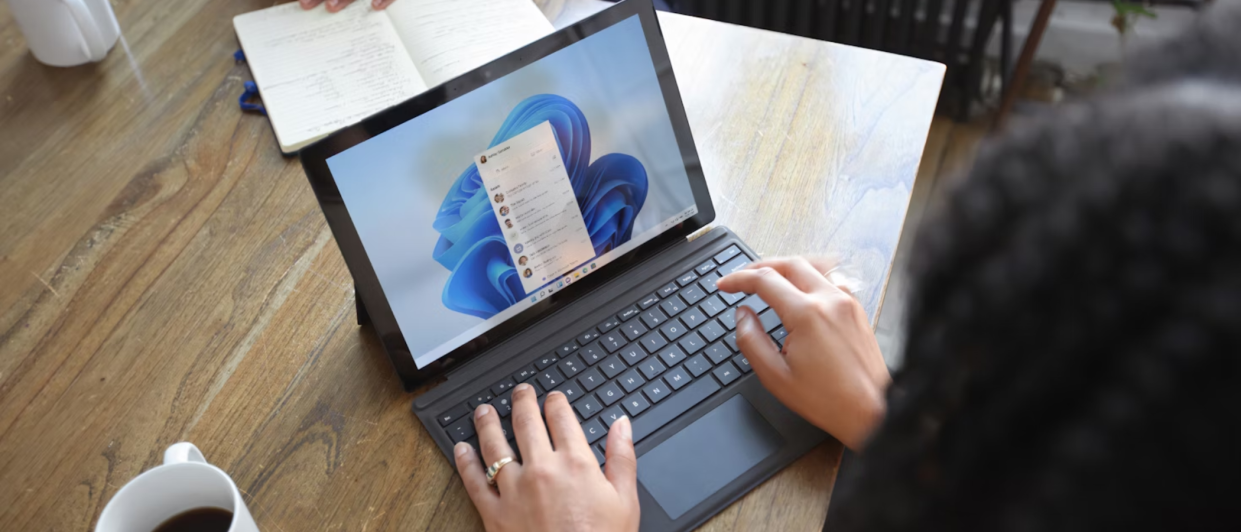  A woman at a table using a Windows laptop, opposite sits a man, neither show their face. 