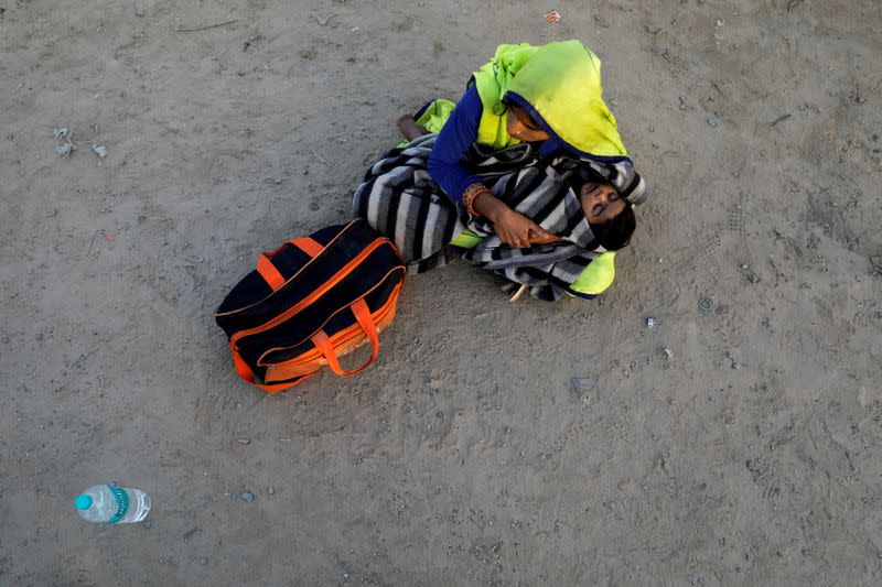 A migrant worker holds her baby as she sits along a highway waiting for a bus to return to their village, during a 21-day nationwide lockdown to limit the spreading of coronavirus disease (COVID-19), in Ghaziabad