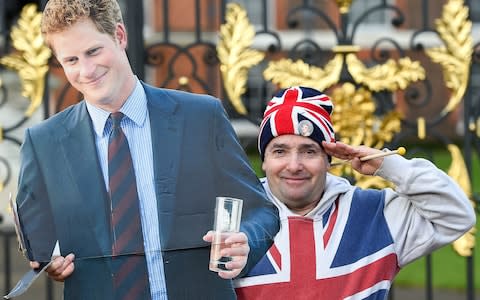 A royalist with a cardboard cutout of Prince Harry salutes at the gates of Kensington Palace - Credit: Pete Maclaine / i-Images 