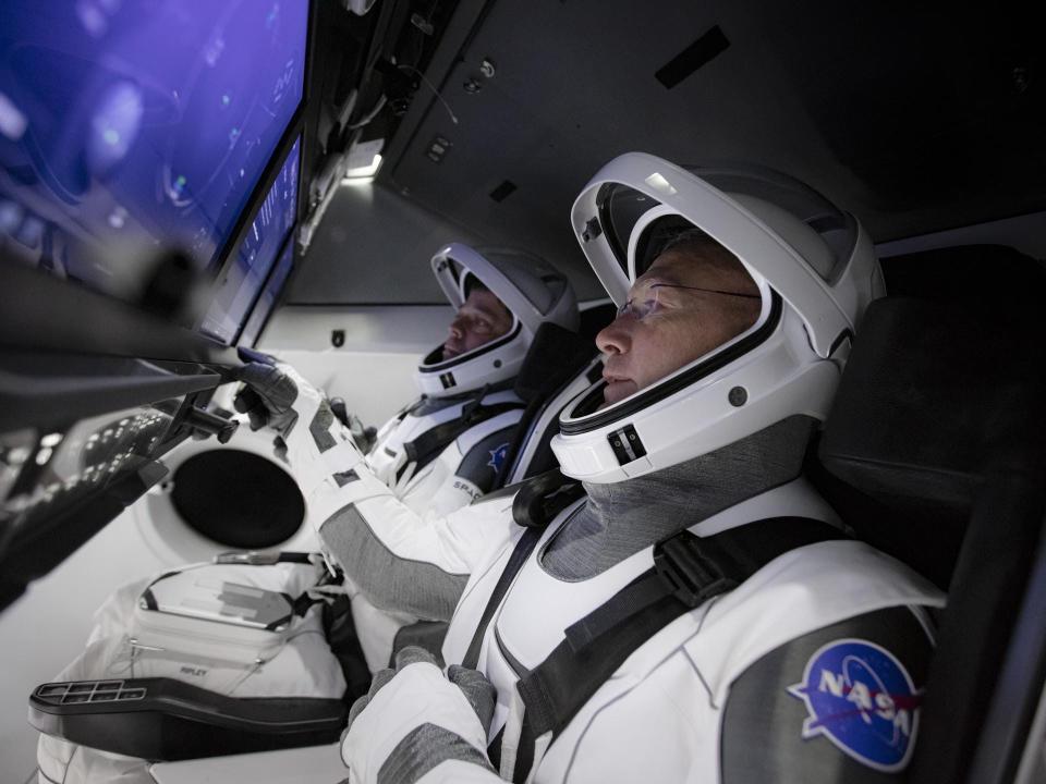 nasa astronauts doug hurley bob behnken in spacex spacesuit sit inside crew dragon capsule in front of blue control screens