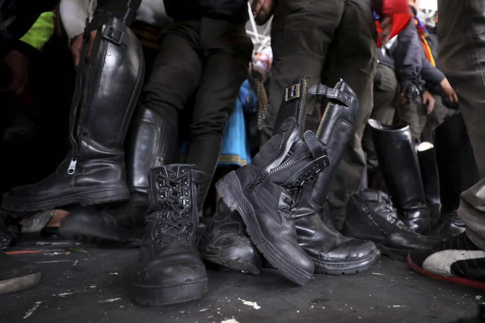 Police officers detained by anti-government protesters are forced to remove their boots on the stage at the Casa de Cultura in Quito, Ecuador, Thursday, Oct. 10, 2019. Indigenous demonstrators in Ecuador are holding captive at least eight police officers following anti-government protests. Ecuador's indigenous groups are gathering for more protests against the removal of fuel subsidies, a step announced by President Lenín Moreno last week. (AP Photo/Fernando Vergara)