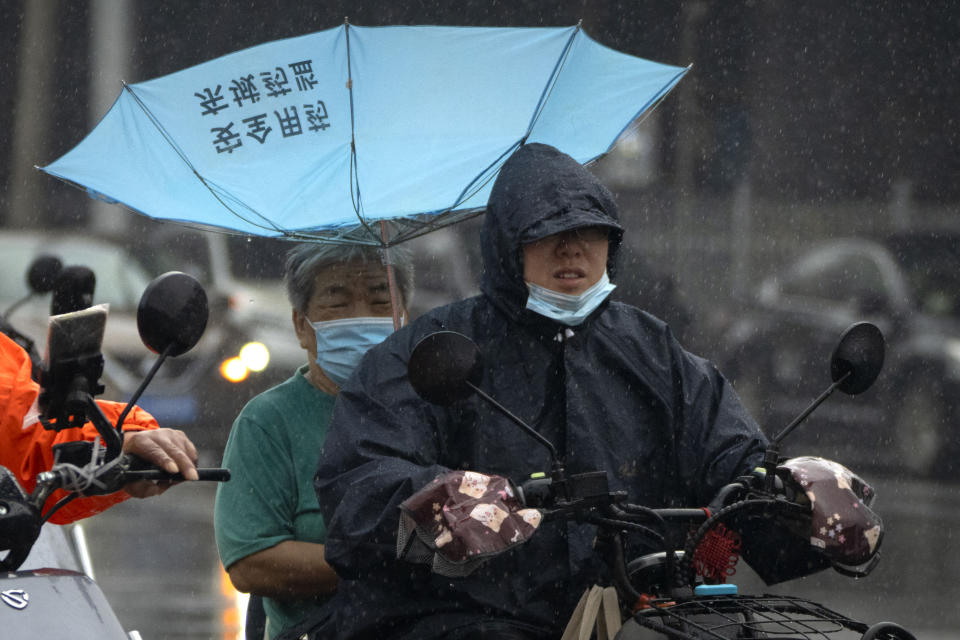 Men wearing face masks ride on a scooter under an upturned umbrella in the rain in Beijing, Thursday, Aug. 18, 2022. Some were killed with others missing after a flash flood in western China Thursday, as China faces both summer rains and severe heat and drought in different parts of the country. (AP Photo/Mark Schiefelbein)