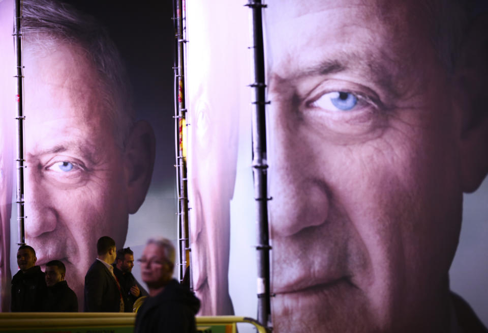 FILE - In this Jan. 29, 2019, file photo, people walk by posters of retired Israeli military chief Benny Gantz before the official launch of his election campaign for the April 2019 elections, in Tel Aviv. Gantz has burst onto the Israeli political scene as the great hope of the country’s shrinking “peace camp” with a message that is anything but dovish. The retired general, who hopes to topple Prime Minister Benjamin Netanyahu in April 9 elections, talks tough. In today’s Israel, his ready-to-rumble rhetoric appears to be the only way to topple the long-serving Netanyahu. (AP Photo/Oded Balilty, File)