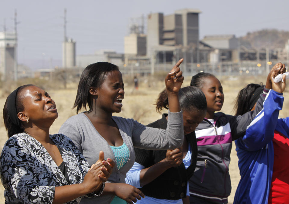 Women from a group of churchgoers wail at the site, Sunday Aug. 19, 2012 at the Lonmin platinum mine, background, near Rustenburg, South Africa, during a memorial service for 34 dead striking miners who were shot and killed by police last Thursday. Miners must return to work Monday or face being fired from the mine where rivalry between unions has exploded into violence. (AP Photo/Denis Farrell)