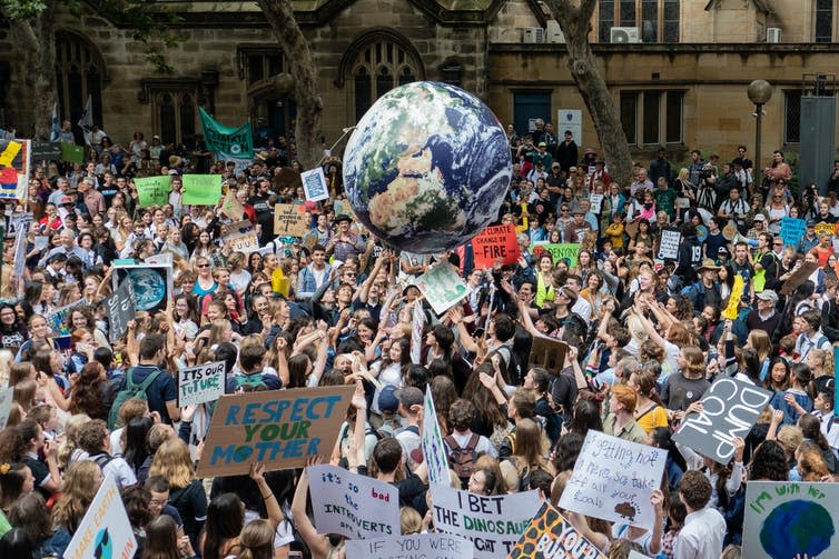 Youth strike demonstrators gather with signs and bounce an inflatable planet Earth.