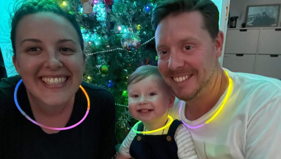 Amy with her partner Clint and son Nicholas in front of a Christmas tree. 