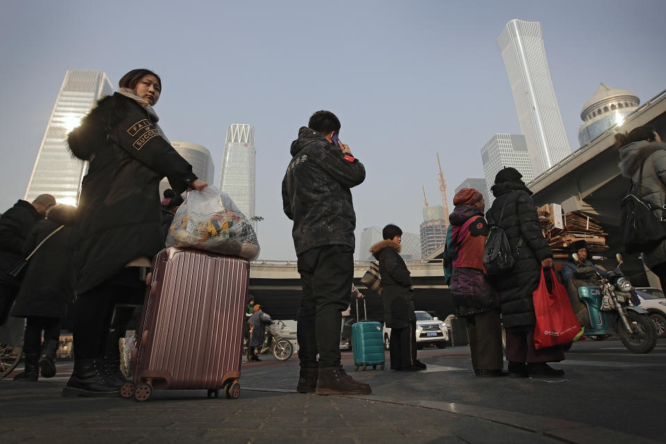 In this Jan. 12, 2019, photo, Chinese people wait to cross a street at the Central Business District in Beijing. China's slowing economy is squeezing the urban workers and entrepreneurs the ruling Communist Party is counting on to help transform this country from a low-wage factory floor into a prosperous consumer market. (AP Photo/Andy Wong)