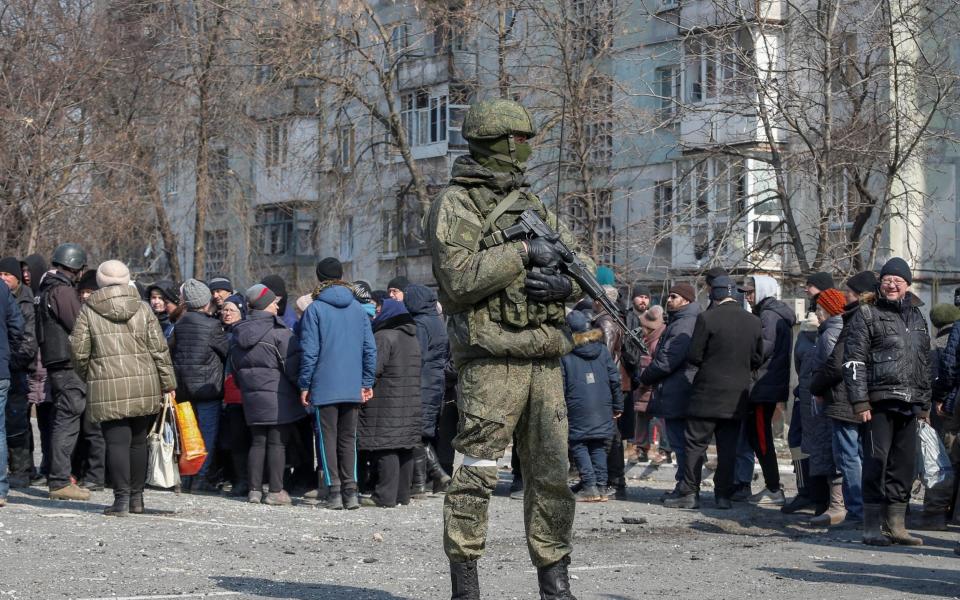 A Russian soldier stands by a queue for humanitarian aid in Mariupol. Russia is reportedly taking thousands of residents from the city hostage - Alexander Ermochenko/Reuters