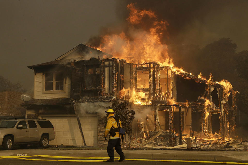 FILE - In this Oct. 9, 2017, file photo, a firefighter walks near a flaming house in Santa Rosa, Calif. An Associated Press review shows widespread problems with the four “public safety power shutoffs” the utility started rolling out in 2018, a year before massive blackouts paralyzed much of California in recent months. Interviews and documents obtained under public records requests reveal persistent failures and broken promises that in some cases compromised public safety. (AP Photo/Jeff Chiu, File)