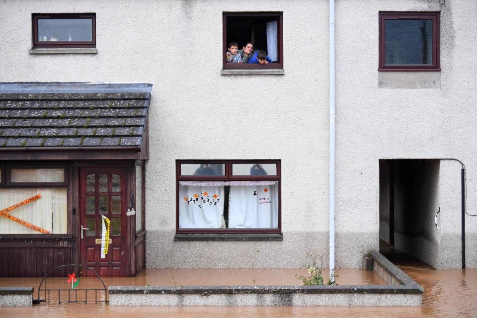 A family trapped in the upper floor of their home look out a window in a flooded stret in Brechin (AFP via Getty Images)
