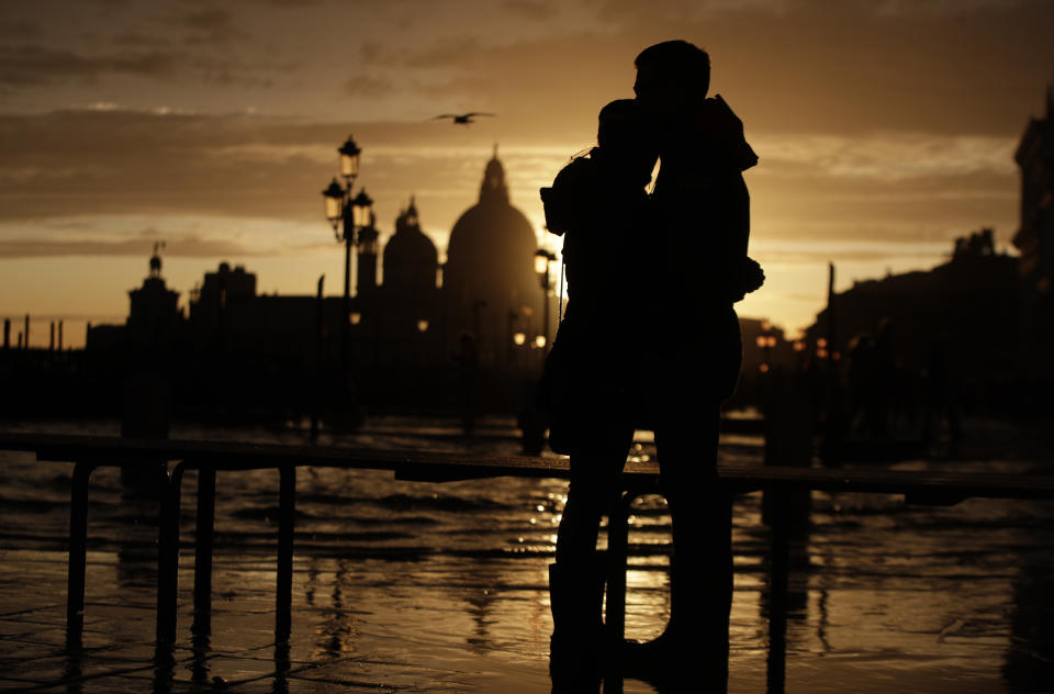 In this photo taken on Sunday, Nov. 17, 2019, a couple stands in a golden sunset in Venice, Italy. Venetians are fed up with what they see as an inadequate to the city's mounting problems: record-breaking flooding, damaging cruise ship traffic and over-tourism. They feel largely left to their own devices, and with ever fewer Venetians living in the historic part of the city to defend its interests and keep it from becoming a theme park or museum. (AP Photo/Luca Bruno)