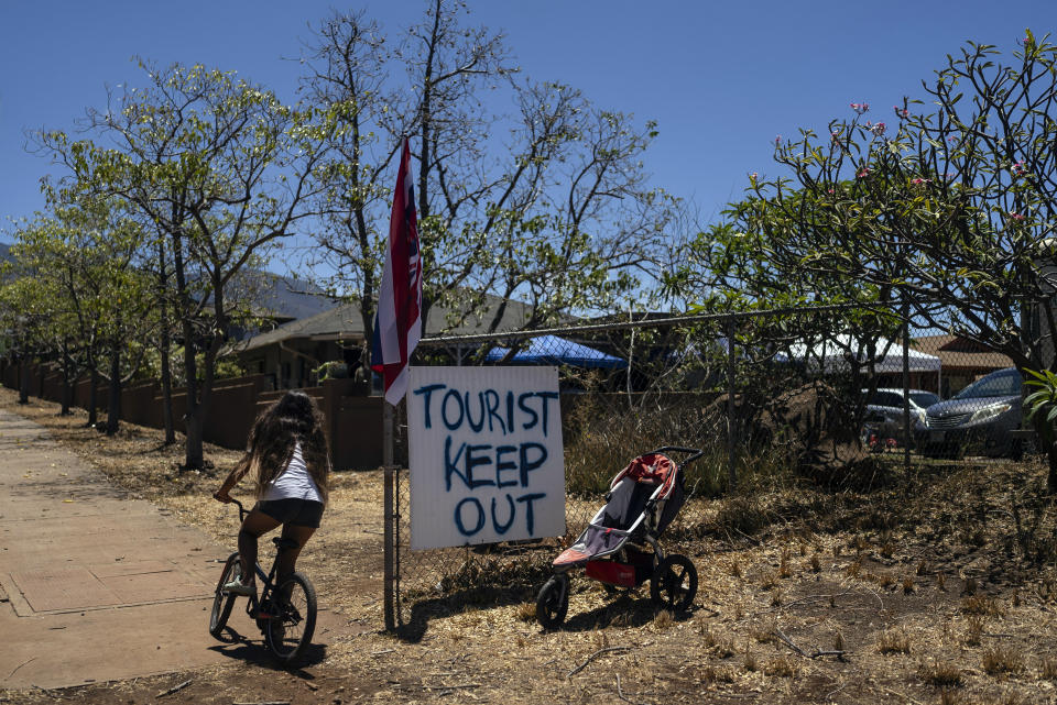 FILE - A girl rides her bike past a sign that says "Tourist Keep Out," in Lahaina, Hawaii, Thursday, Aug. 17, 2023. Nearly a month after the deadliest U.S. wildfire in more than a century killed scores of people, authorities on Maui are working their way through a list of the missing that has grown almost as quickly as names have been removed. Lawsuits are piling up in court over liability for the inferno, and businesses across the island are fretting about what the loss of tourism will mean for their futures. (AP Photo/Jae C. Hong, File)