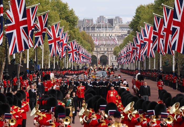 A crowd of buckingham palace guards in a uk-flag adorned caravan for the queen's funeral