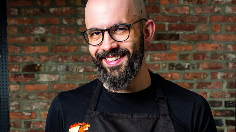 Andrew Rea standing in front of brick wall in lack apron