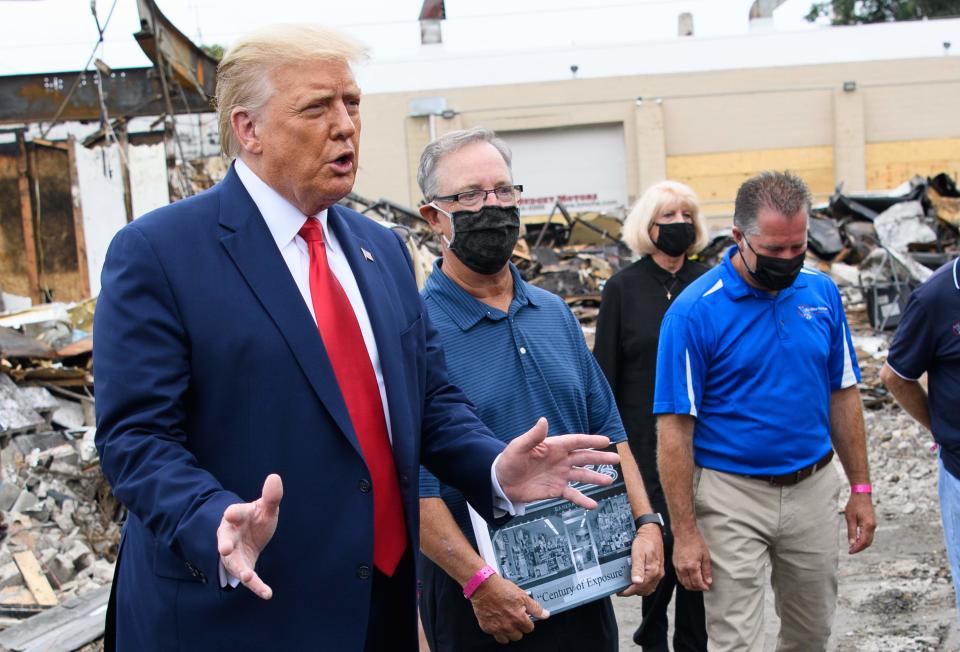 US President Donald Trump speaks to the press as he tours an area affected by civil unrest in Kenosha, Wisconsin on September 1, 2020, as John Rode(C), the former owner of Rode's Camera Shop looks on holding a sign.