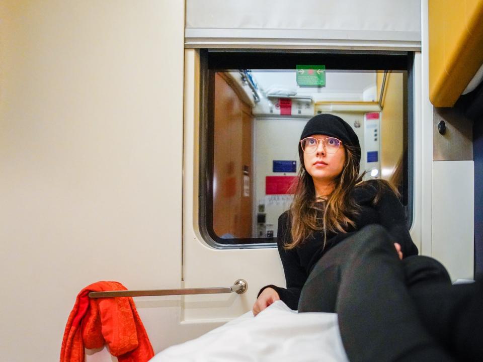 The author sits on a white bunk inside an overnight train cabin with a dark window behind her.