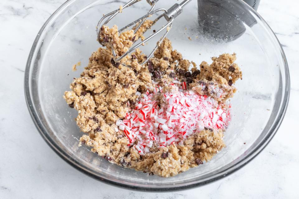 Crushed peppermint and chocolate chunks on top of cookie dough in glass bowl