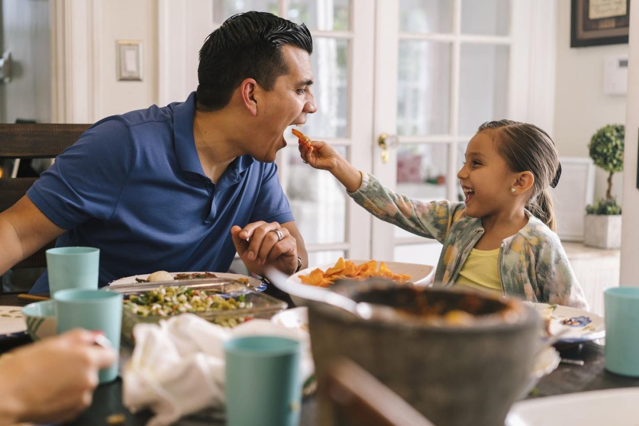 young girl feeding her father at dinner table