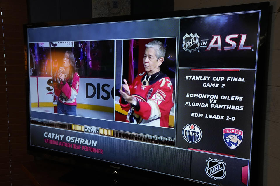 Gina Miles winner of season 23 of The Voice, left, sings and Cathy Oshrain signs the national anthem during the Stanley Cup hockey final, seen on a television, Monday, June 10, 2024 in Genoa Township, Mich. Bob Madden is deaf and he was enjoying the view with access to the commentary delivered in American Sign Language for the first time during a sporting event. The NHL became the first major sports league to offer play by play and analysis in ASL during a live broadcast. (AP Photo/Carlos Osorio)