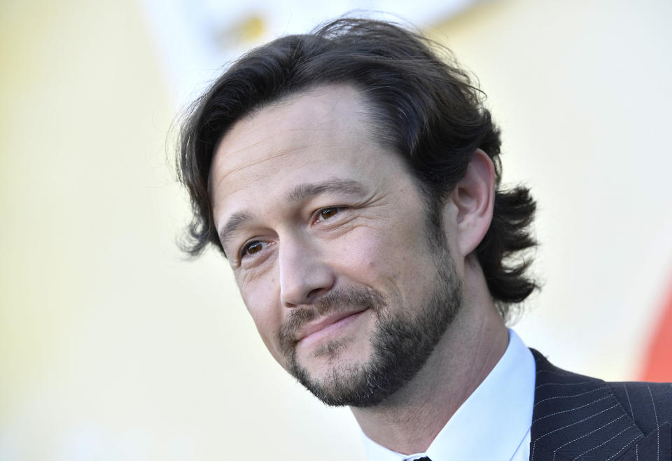 Joseph Gordon-Levitt, wearing a pinstripe suit and white shirt, smiles at an event