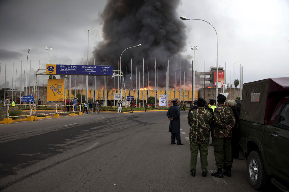 Policemen stand guard as fire rages at the International arrivals unit of Jomo Kenyatta International Airport, Nairobi, Kenya, Wednesday, Aug. 7, 2013. A massive fire engulfed the arrivals hall at Kenya's main international airport early Wednesday, forcing East Africa's largest airport to close and the rerouting of all inbound flights. Dark black smoke that billowed skyward was visible across much of Nairobi as emergency teams battled the blaze. (AP Photo/Sayyid Azim)