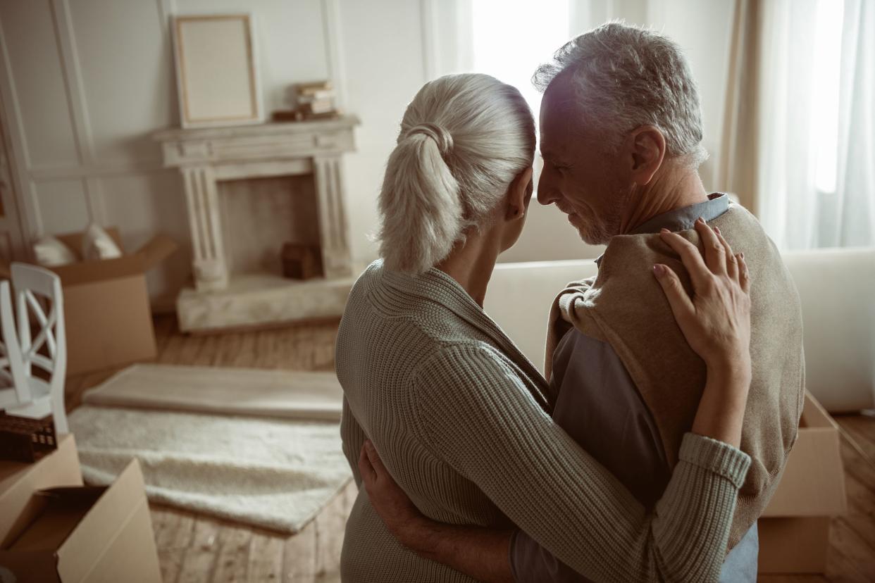 tender senior husband and wife embracing and looking at their home