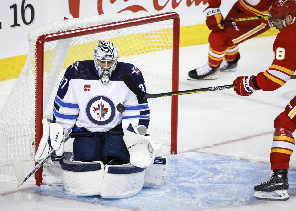 Winnipeg Jets goalie Connor Hellebuyck, left, gets hit by the stick of Calgary Flames forward A.J. Greer during the first period of an NHL hockey game Wednesday, Oct. 11, 2023, in Calgary, Alberta. (Jeff McIntosh/The Canadian Press via AP)