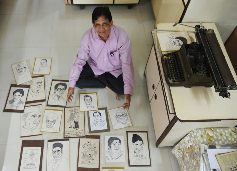 Indian artist Chandrakant Bhide poses with artwork showing portraits of public figures and deities that he created using a typewriter