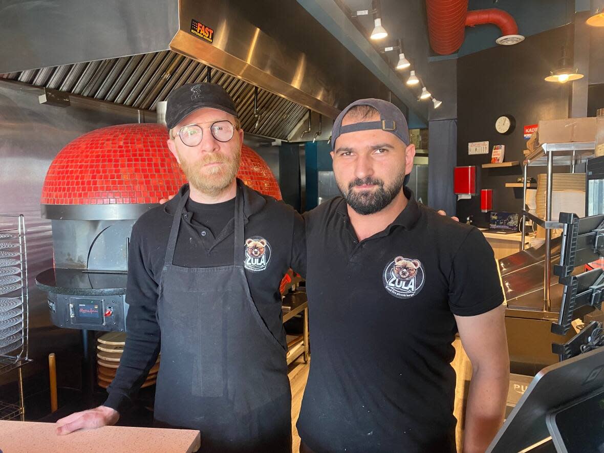 Zaza Pervane, left, and Muhammet Yildirim, right, work at Zula Burger and Pizza, a west-end Toronto take-out spot. They say they're stuck watching from afar as friends and family deal with a devastating earthquake back home in Turkey.  (Talia Ricci/CBC - image credit)