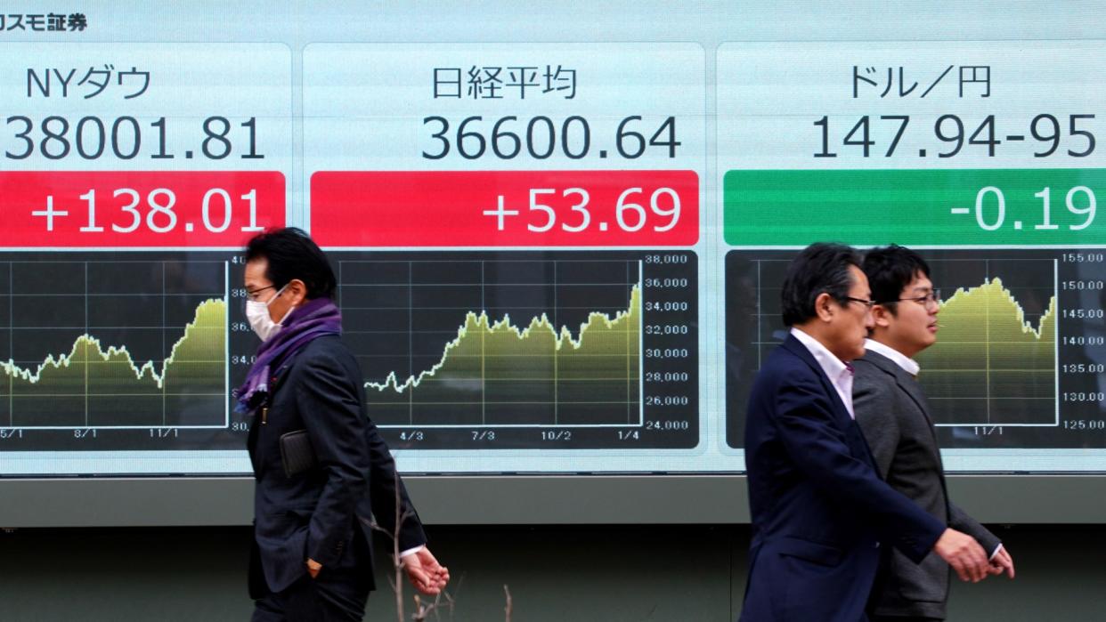  Pedestrians walk past a board with Japanese stocks. 