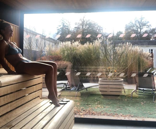 helen sits in a partially lit sauna wearing a bikini