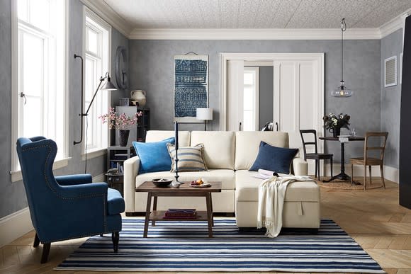 Furnished room with a blue armchair, tan couch, and blue-and-tan rug.