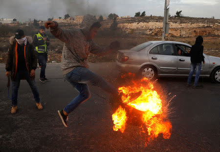 A Palestinian kicks a burning tire during clashes with Israeli troops at a protest against U.S. President Donald Trump's decision to recognize Jerusalem as Israel's capital, near the Jewish settlement of Beit El, near the West Bank city of Ramallah December 10, 2017. REUTERS/Mohamad Torokman