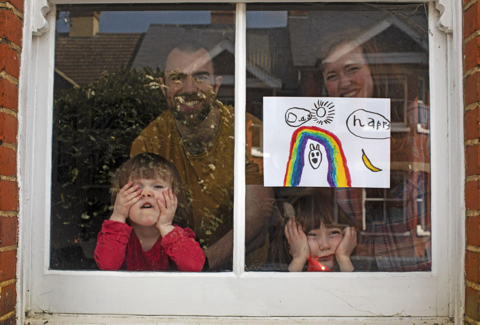 FILE - In this Saturday, April 4, 2020 file photo Amelie and her sister Camille watch from their front window as the lockdown enters it's third week along with their parents Victoria and Damian Kerr in Berkhamsted, England. (AP Photo/Elizabeth Dalziel, File)