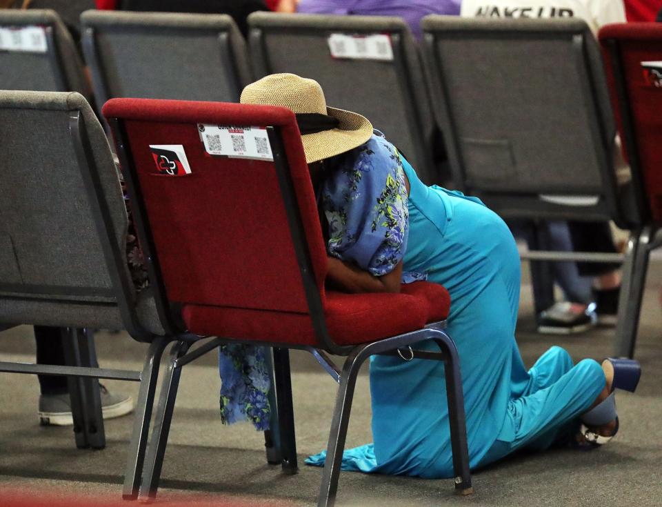 A woman kneels at her seat for a moment of prayer before a unity gathering at The Remedy Church.