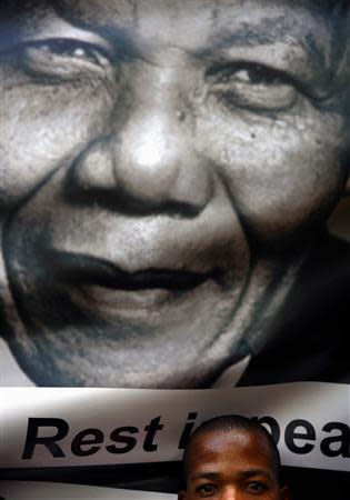 A mourner peers under a portrait of Nelson Mandela People soon after the coffin of former South African President Nelson Mandela travelled through a street in Pretoria, December 11, 2013, on its way to the Union Buildings, where his coffin will lie in state for three days. REUTERS/Yannis Behrakis