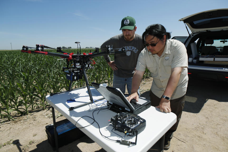 In this Thursday, July 11, 2019, photograph, United States Department of Agriculture intern Alex Olsen, left, and engineering technician Kevin Yemoto work to set up a drone for flight over a research farm northeast of Greeley, Colo. Researchers are using drones carrying imaging cameras over the fields in conjunction with stationary sensors connected to the internet to chart the growth of crops in an effort to integrate new technology into the age-old skill of farming. (AP Photo/David Zalubowski)